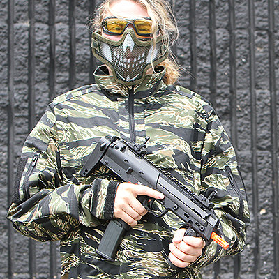 Airsoft player with valken eye protection and airsoft mesh mask wearing tiger strip camo and holding HK MP7 airsoft gun